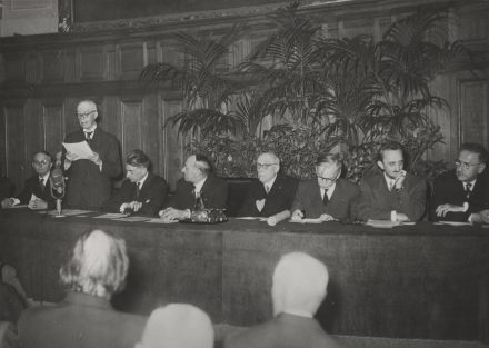 Discours de Louis de Broglie avec Jean Berthouin et Francis Perrin à la tribune pour le 20e anniversaire de la découverte de la radioactivité artificielle à la Sorbonne, octobre 1954